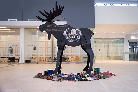 a large wooden moose with Truth and Reconciliation written on it, surrounded by childrens' shoes
